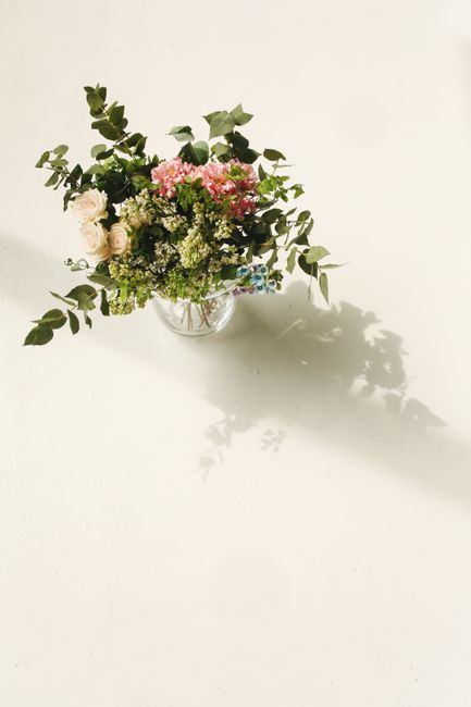 A delicate floral arrangement placed in a clear glass vase, featuring a mix of fresh flowers including pale pink roses, white and green hydrangeas, and small blue and white blooms, complemented by lus
