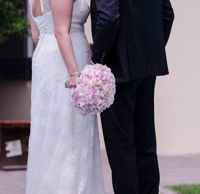 A close-up view of a bride and groom standing side by side during a wedding ceremony at Pitzhanger Manor, with the bride holding a bouquet arrangement of blush pink roses and hydrangeas. The bride wea